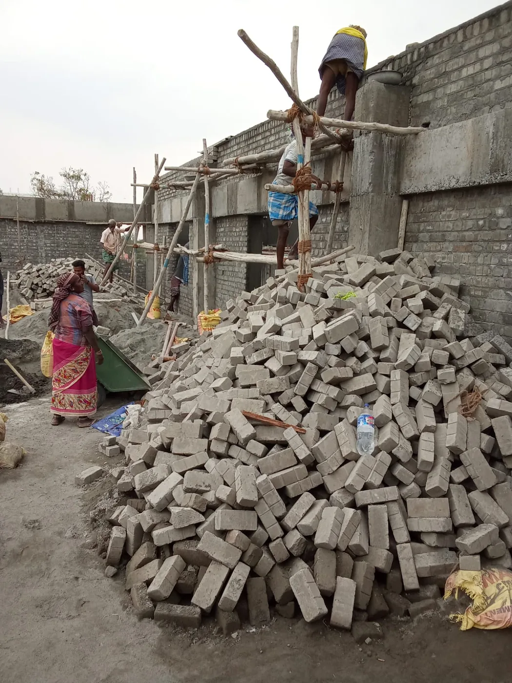 Masons building a brick wall with concrete blocks stacked on site